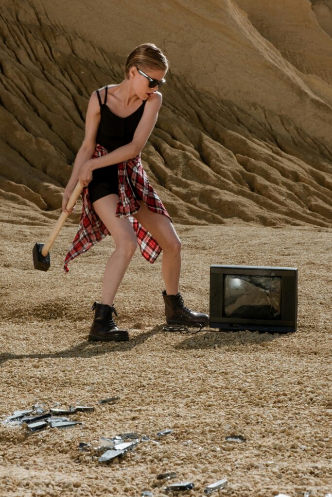 Woman in a desert smashing an old TV with a sledgehammer, showcasing empowerment.